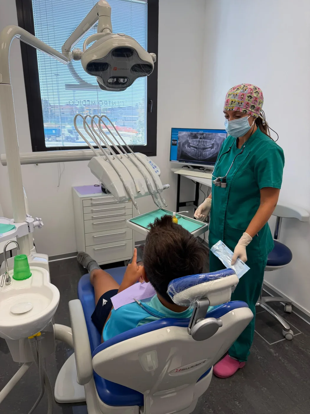 La Dott.ssa Giorgia mostra al bambino, seduto sulla poltrona, la bustina sigillata con gli strumenti prima di aprirla